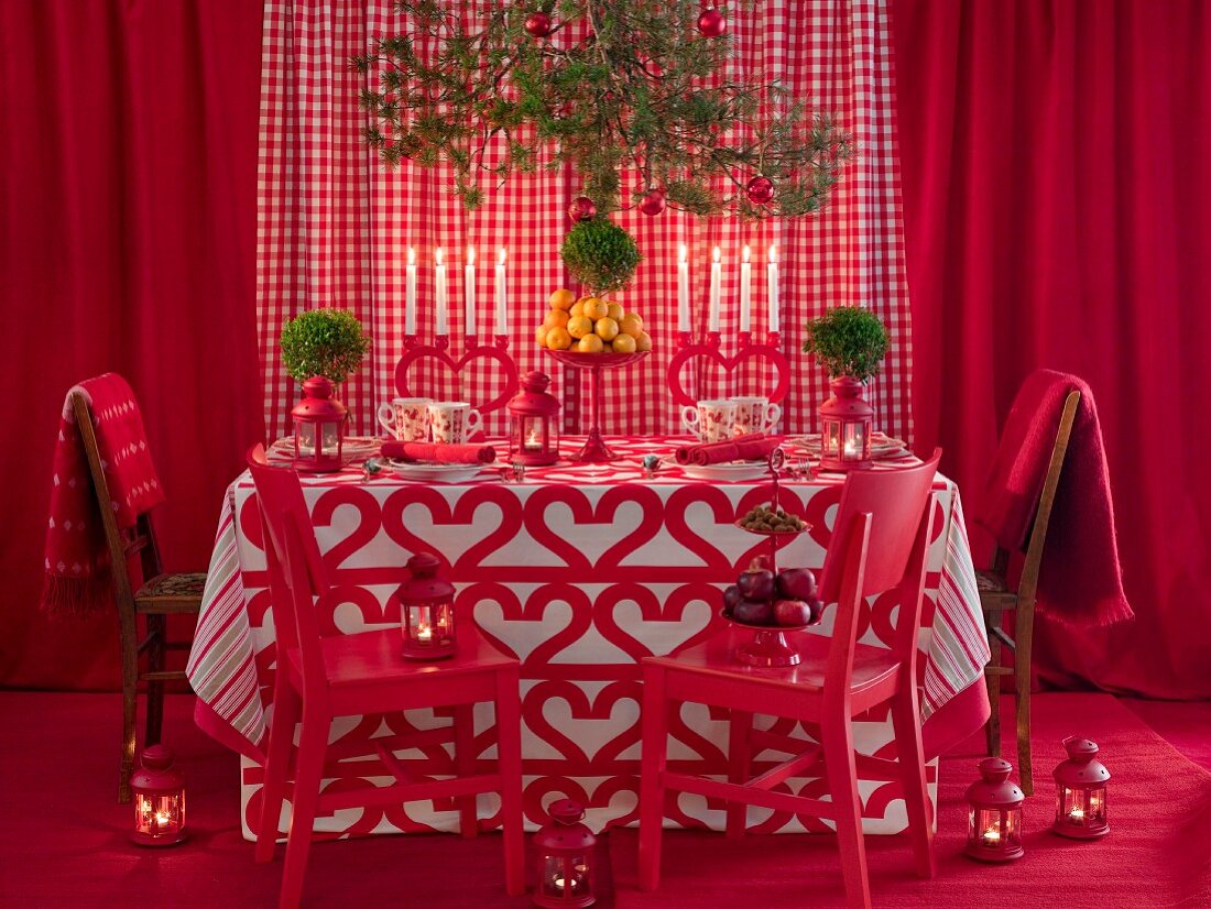 Esstisch mit Decke und Kerzenständern im Herzdesign, umgeben von roten Dekoelementen