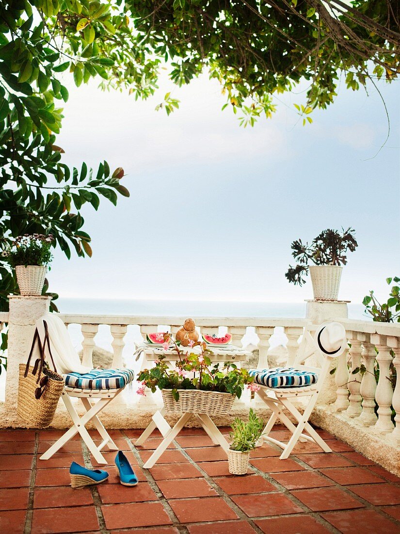 Kleiner Tisch mit zwei Stühlen vor Balustrade auf Terracotta-Terrasse mit Meerblick