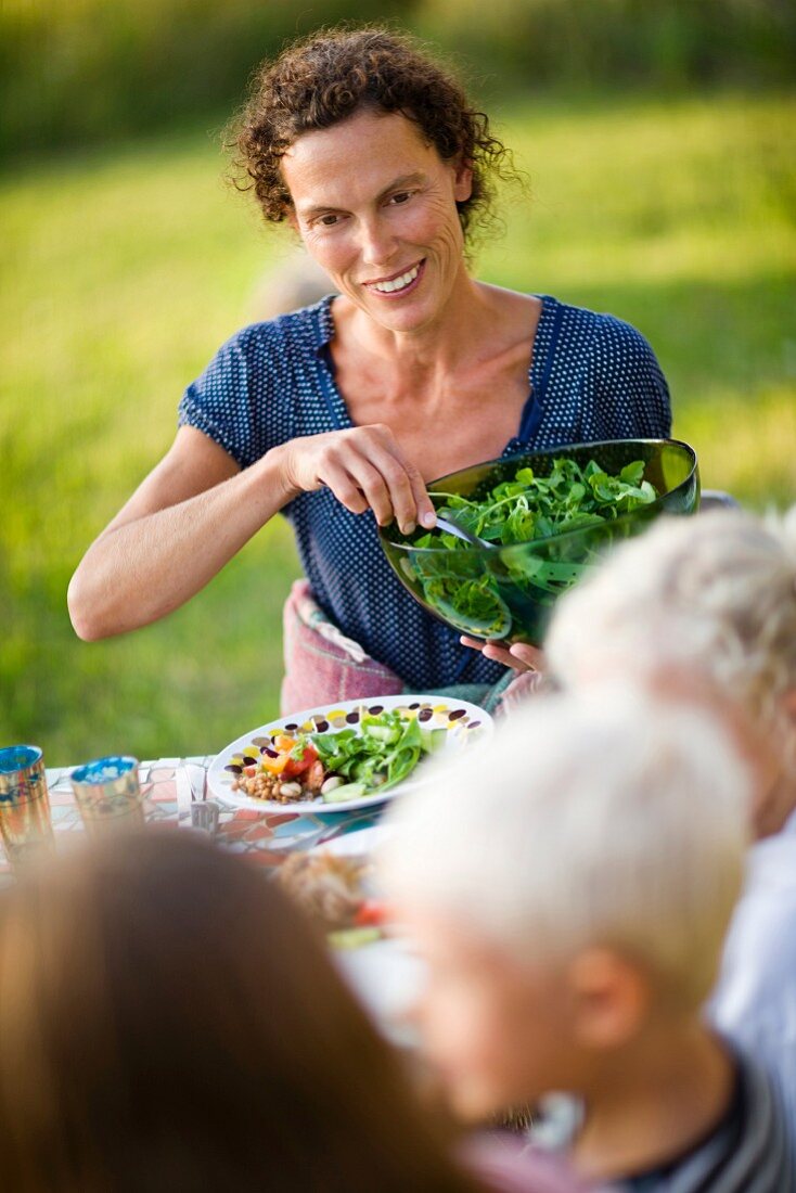 Frau verteilt Salat an Tisch im Freien