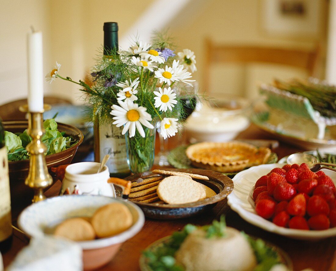 Schälchen mit Keksen und Erdbeeren, Margeritenstrauss und Kerzenständer auf einem Esstisch