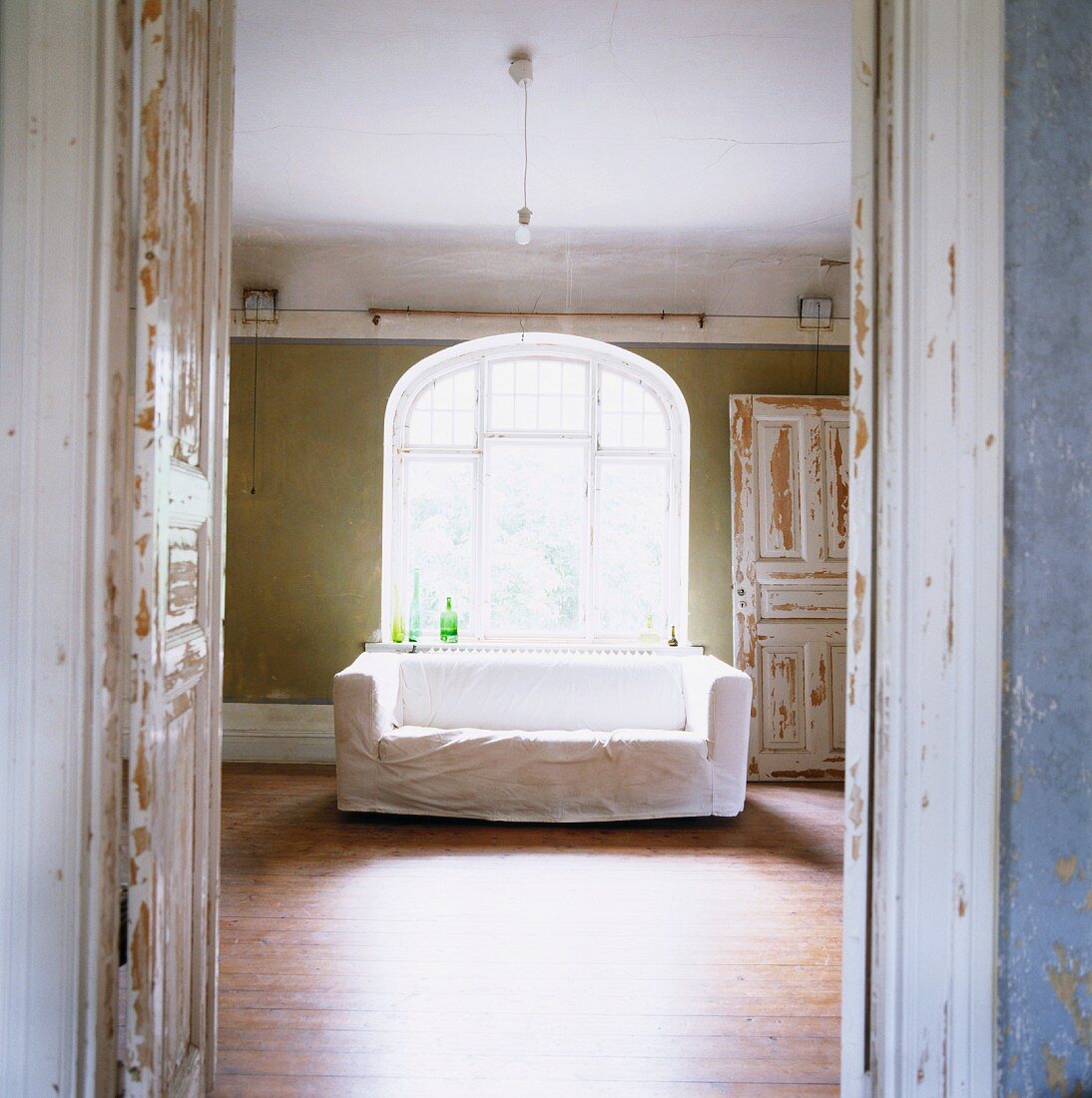 Blick durch offene Tür auf Sofa mit weisser Husse am Fenster mit Rundbogen in Vintage Ambiente