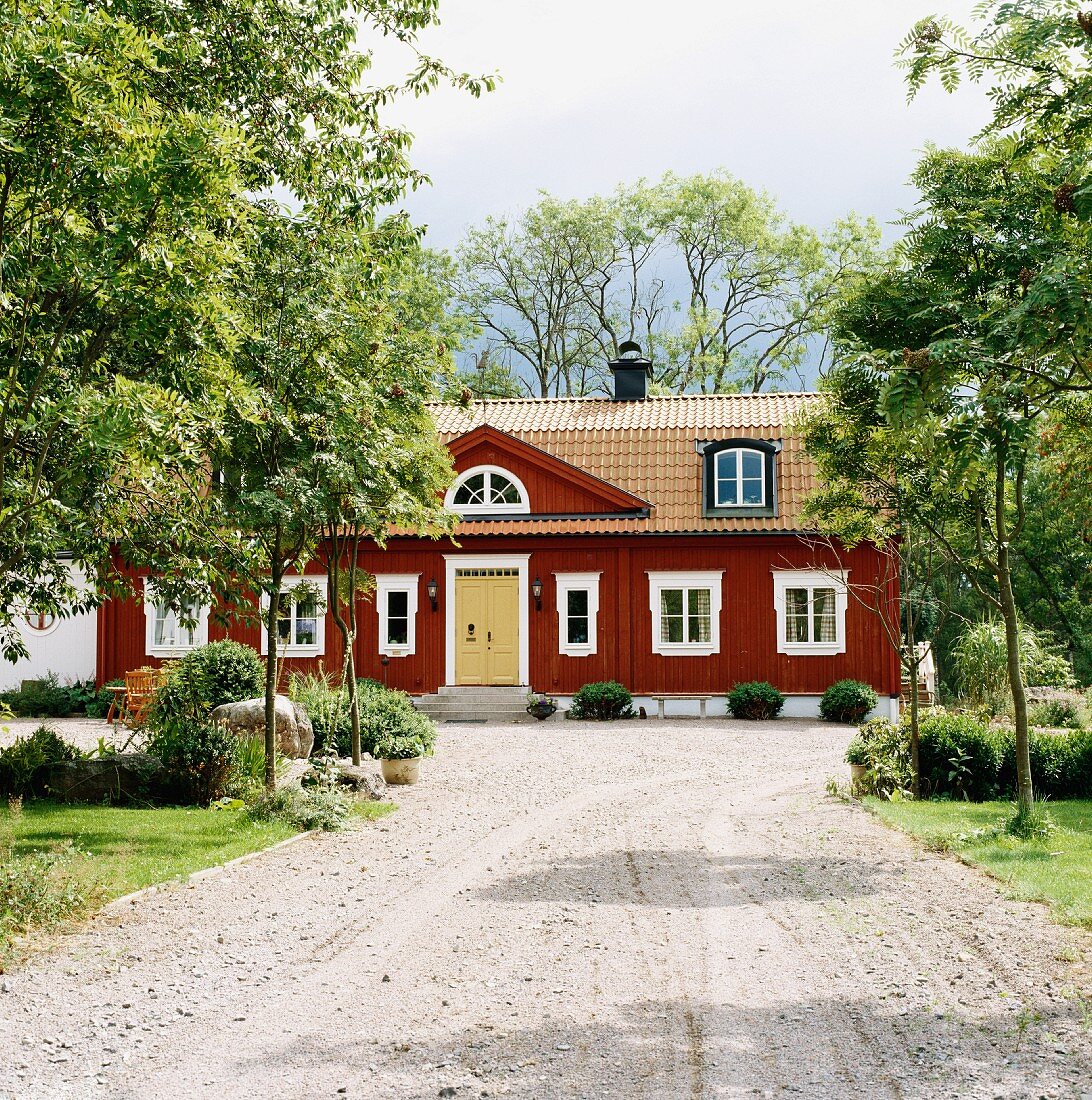 Breiter Kiesweg zu altem, schwedischem Holzhaus mit Portikus über dem Eingang