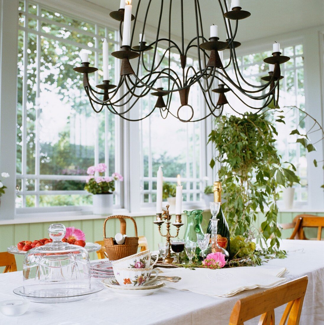 Wrought iron chandelier above white, set table in window bay
