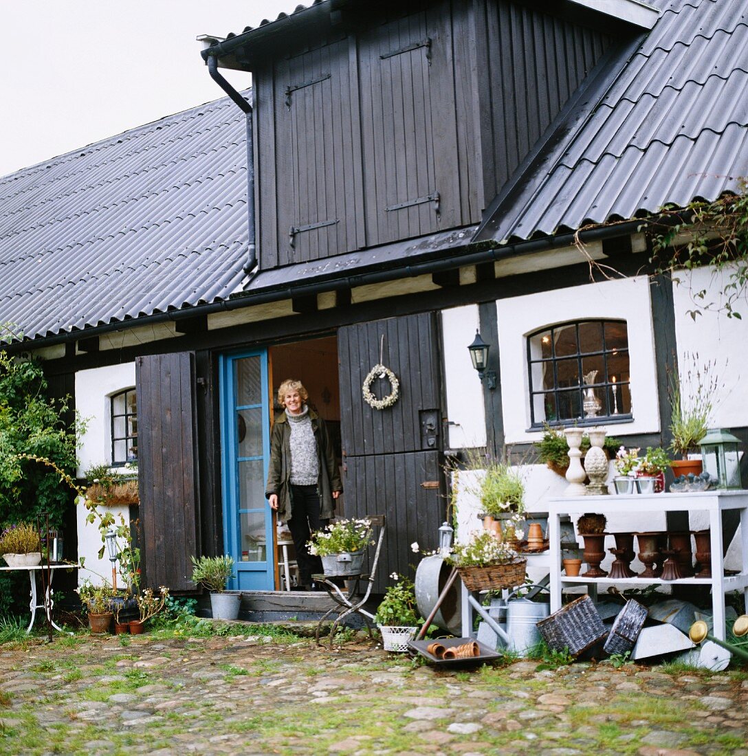 Woman in entrance of half-timbered house flanked by hodgepodge of planters, garden decorations and zinc containers