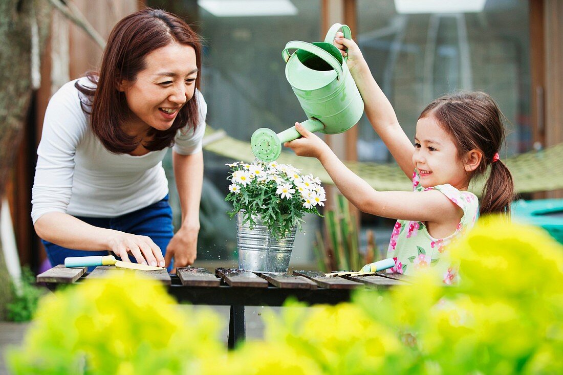 Mutter und Tochter am Tisch im Freien beim Blumengiessen