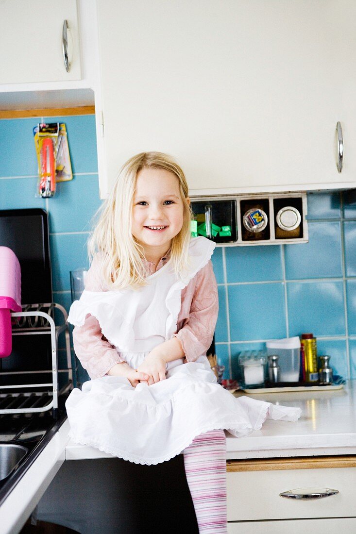 Lachendes, kleines Mädchen sitzt auf Küchenarbeitsplatte vor blauen Fliesen