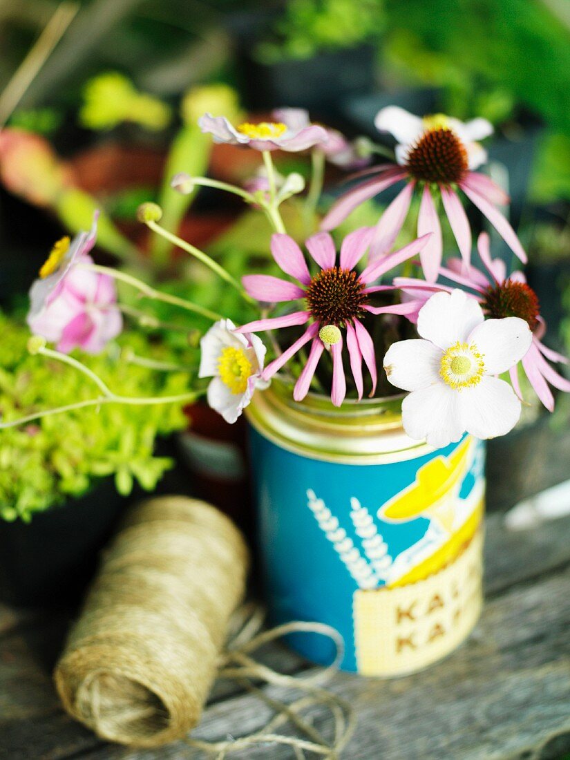 Vintage Dose als Vase für Sonnenhut- und Windröschenblüten auf einem Gartentisch