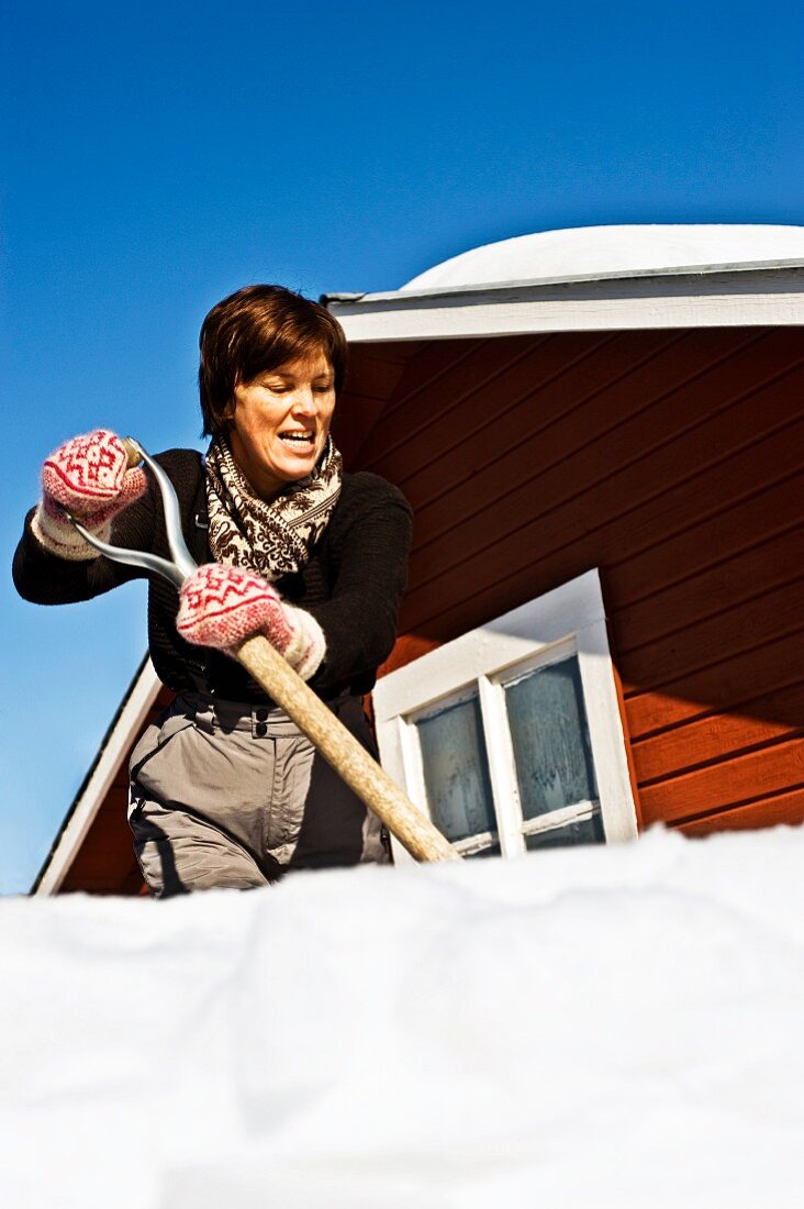 A woman shovelling snow from a roof, Sweden