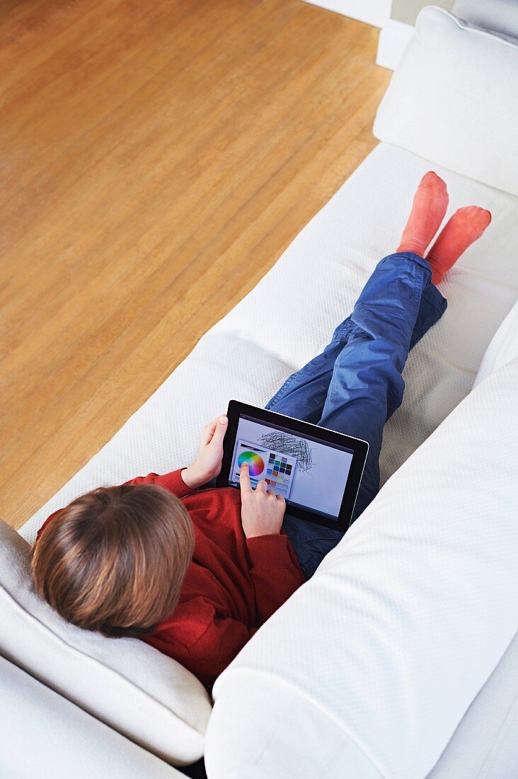 Junge auf weißem Sofa liegend mit Tablet