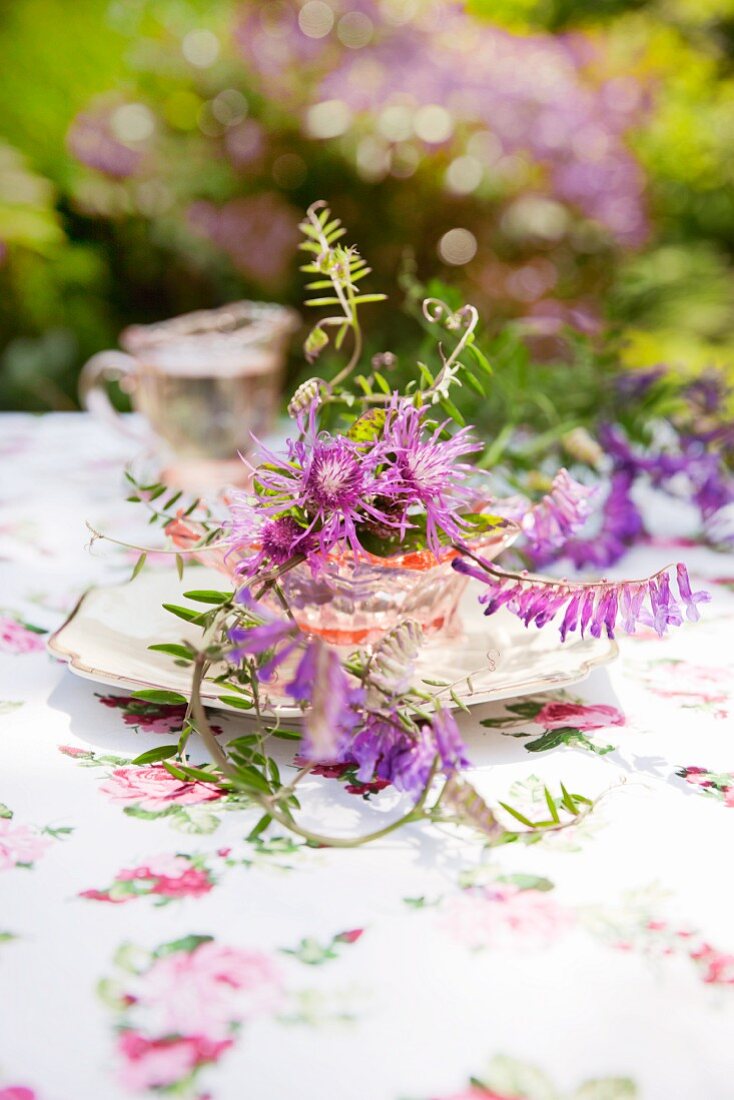 Wiesenblumen in alter Glasschale auf altem Teller als Tischdeko im Freien
