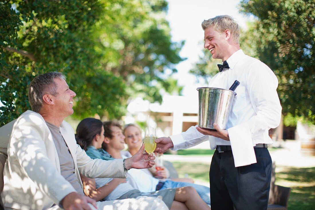 Kellner mit silbernem Weinkühler bedient Geschäftsleute im Freien