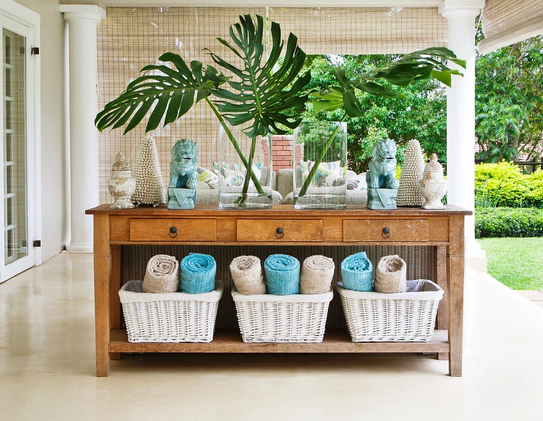 Spa oasis - rolled towels in baskets below rustic wooden console table on veranda of colonial-style villa