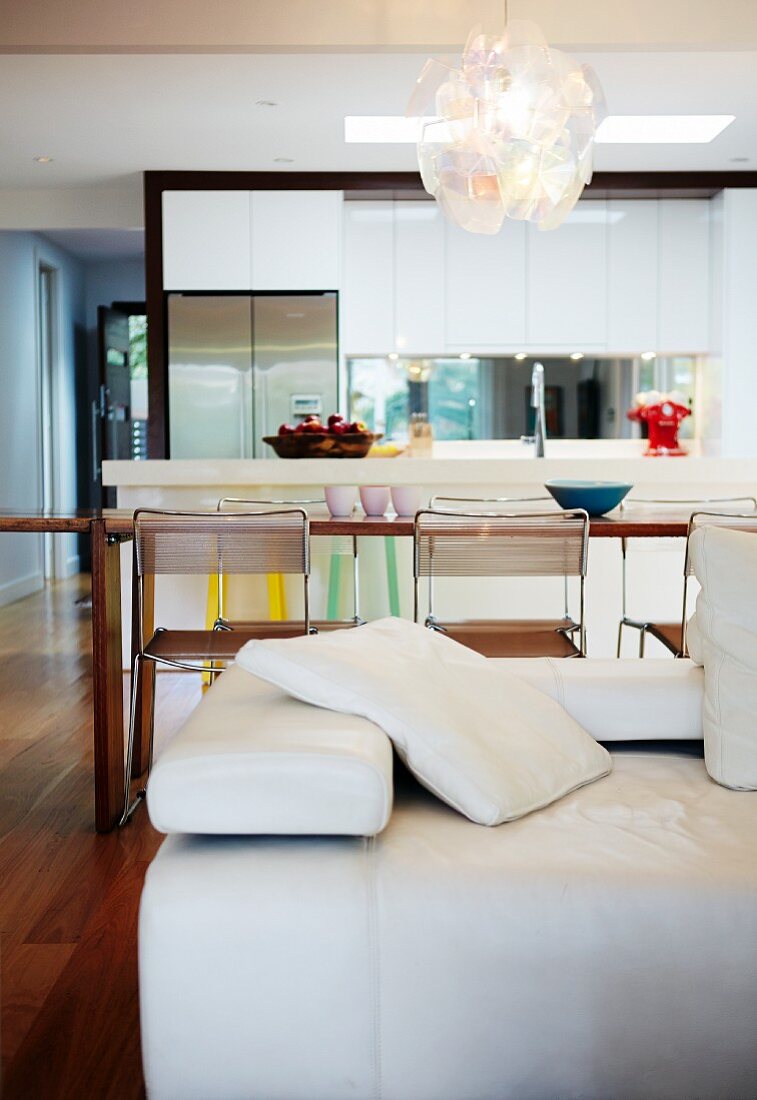 Partially visible white leather couch in front of dining area and open-plan kitchen in modern setting