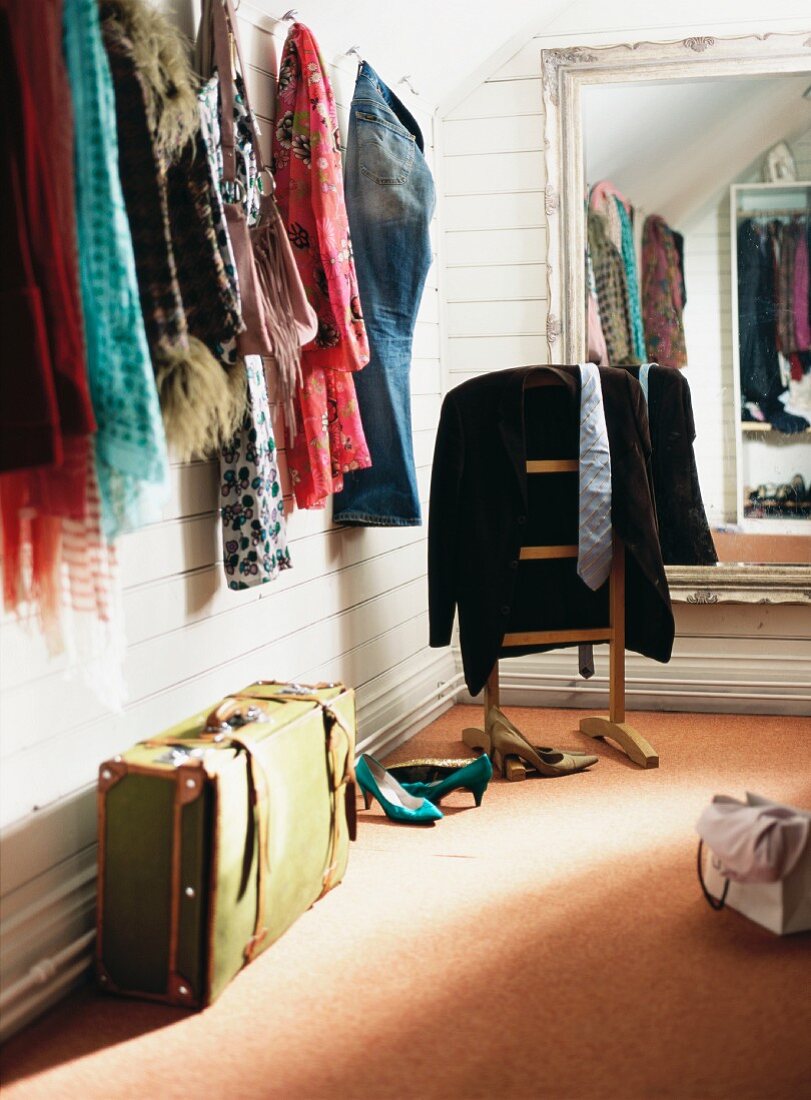 Verschiedene Halstücher an Wandhaken und Vintage Koffer vor stummen Diener am Wandspiegel in holzverkleideter Ankleide