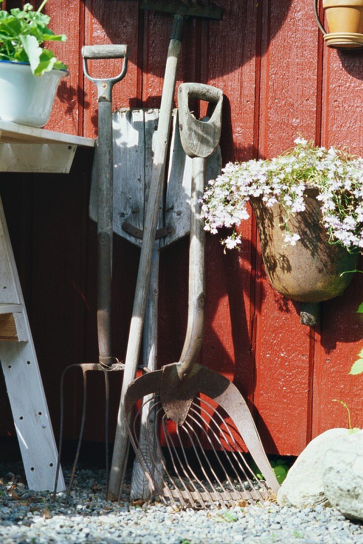 Vintage Gartengeräte und aufgehängter Blumentopf an rotbrauner Holzwand