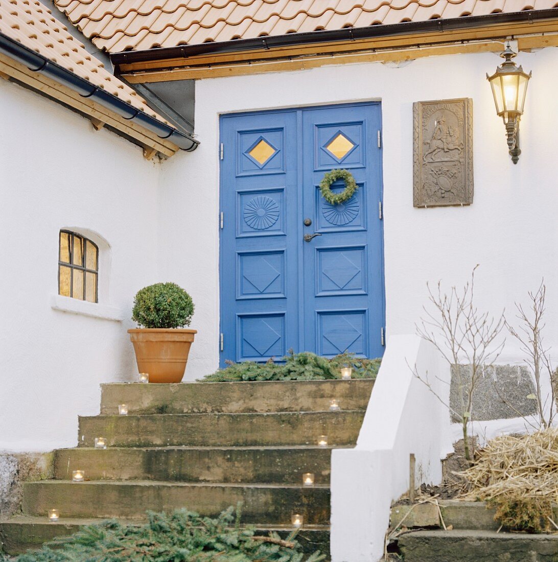Steintreppe mit Windlichtern vor blau gestrichener Eingangstür eines Wohnhauses