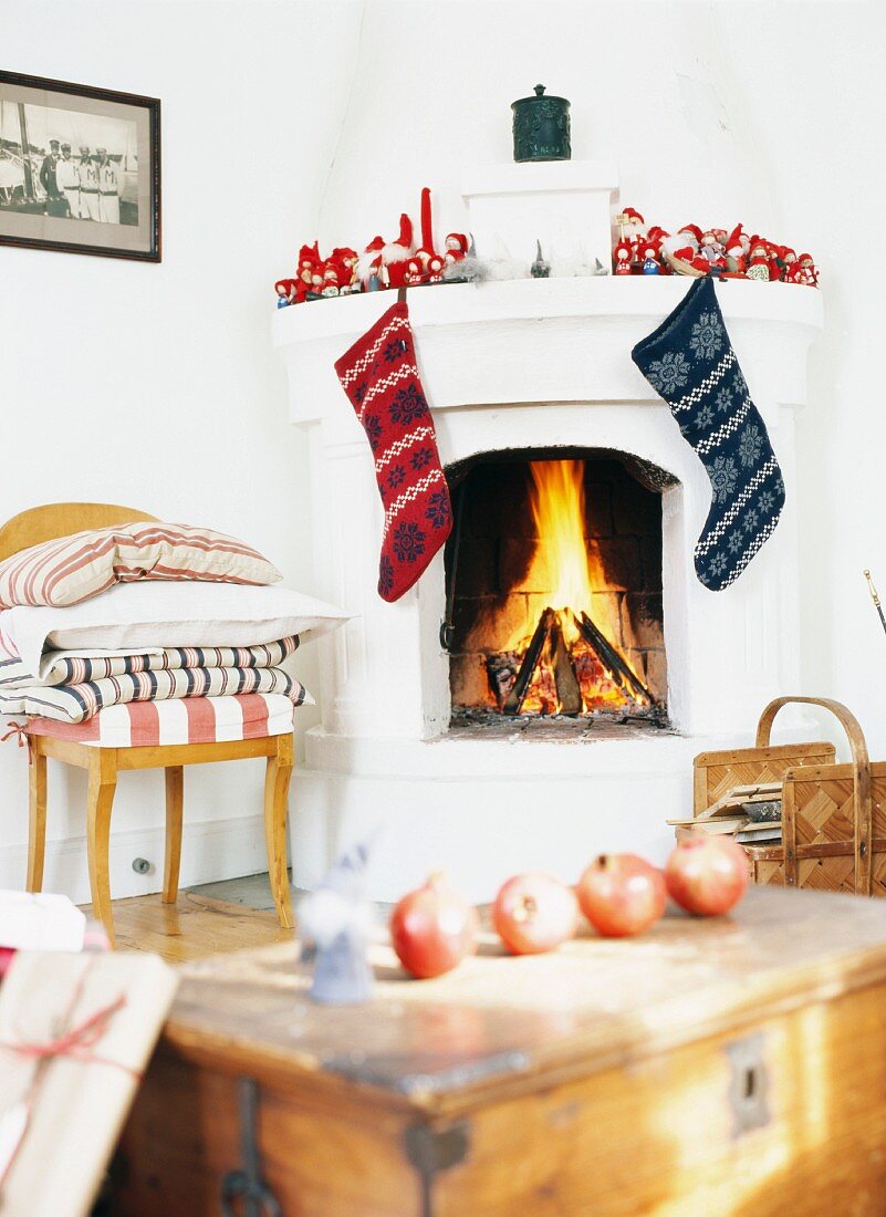 Granatäpfel auf Holztruhe und weihnachtlich dekorierter Kamin mit Feuer