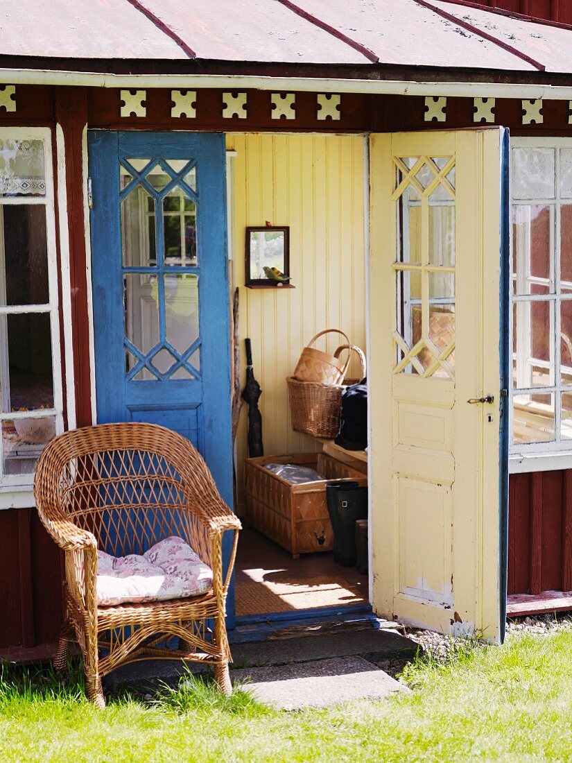 Wicker chair in front of open door of wooden cottage