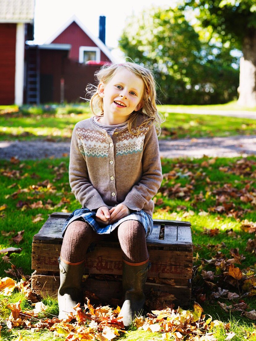 Girl sitting on wooden crate in autumnal garden