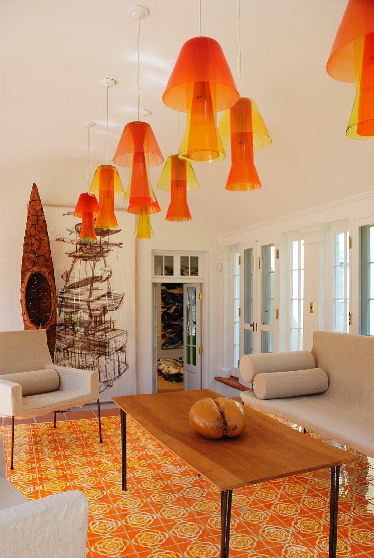 Wohnraum mit in Reihe gehängten Deckenleuchten aus gelborange getöntem Acrylglas und gleichfarbigen Bodenfliesen
