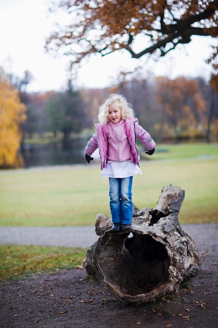 Kleines Mädchen balanciert auf einem hohlen Holzklotz