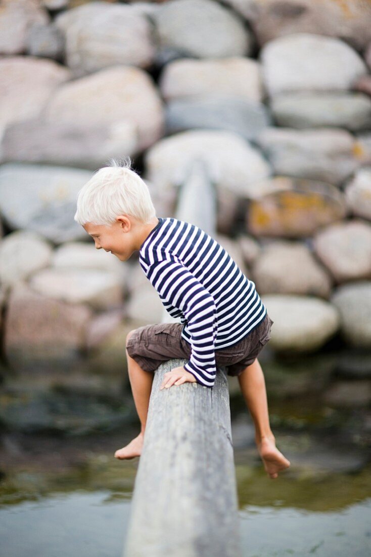 Kleiner Junge auf einem Holzstamm balancierend und ins Wasser schauend
