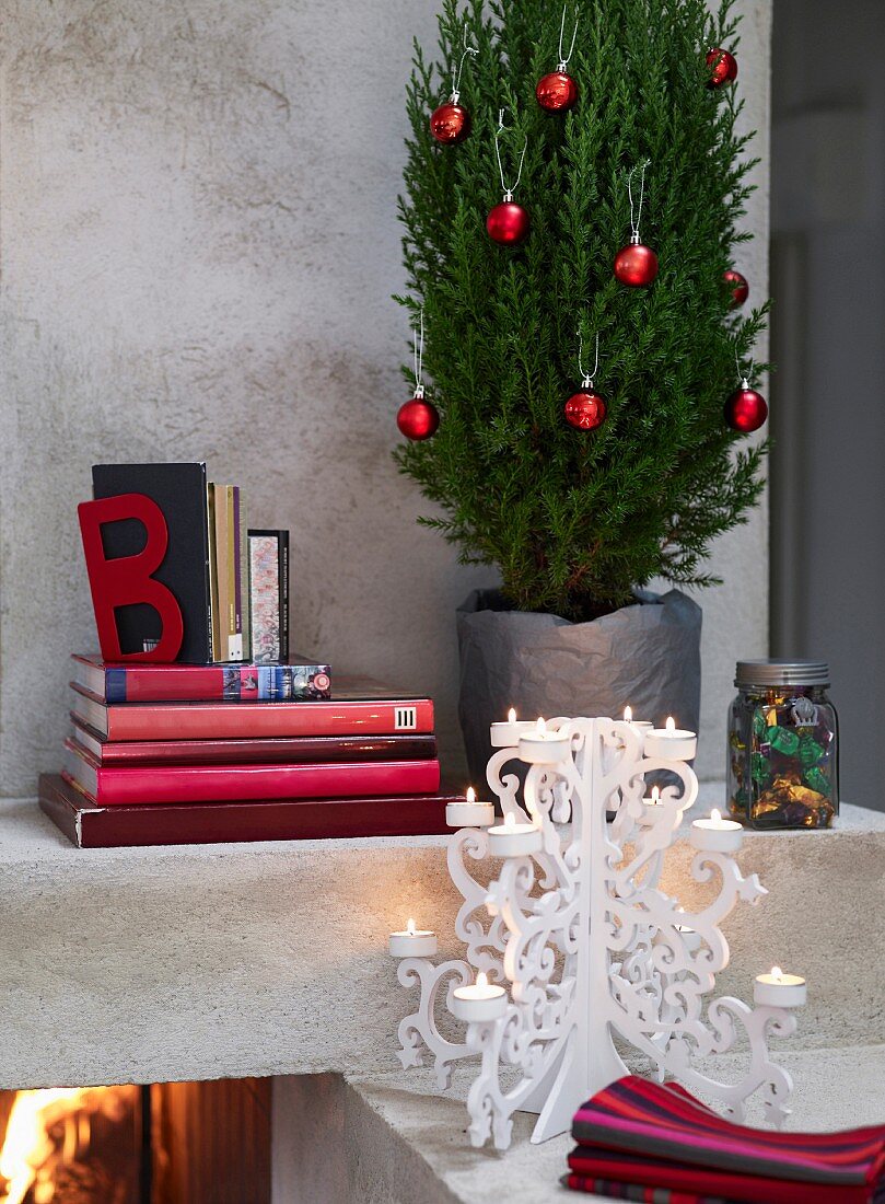 Weihnachtlich geschmückte Topfpflanze neben Bücherstapel und weißem Kerzenhalter auf Kaminsims