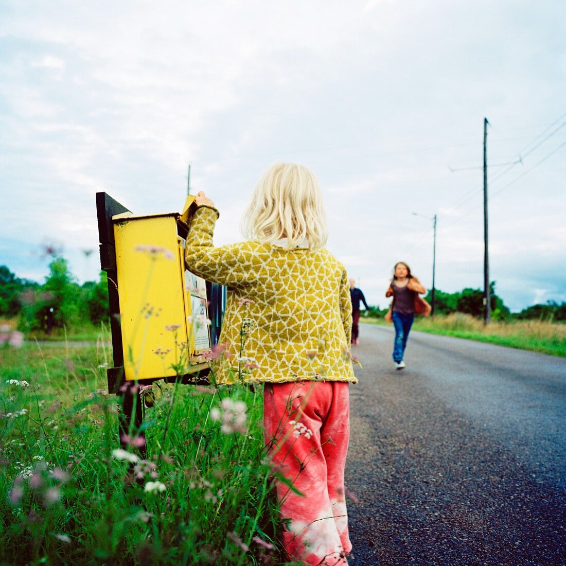 Blondes Mädchen schaut nach Post in Briefkasten an der Landstraße