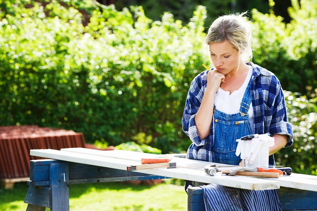 Frau beim Planen von Renovierungsarbeiten nachdenklich vor einem provisorischen Arbeitstisch im Garten