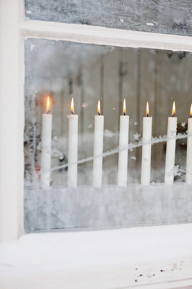 Blick auf brennende Kerzenreihe hinter vereistem Fenster