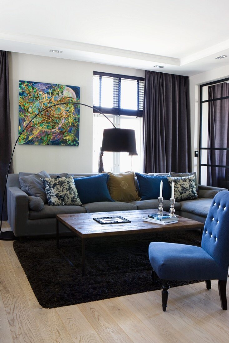 Chair with blue upholstery and turned legs, coffee table in front of sofa and arc lamp in corner of living room