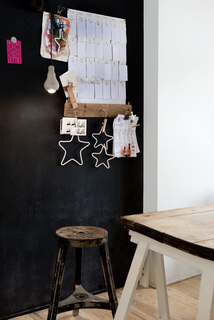 Vintage stool and old wooden table top on white trestles in front of black-painted pinboard with paper notes and stars