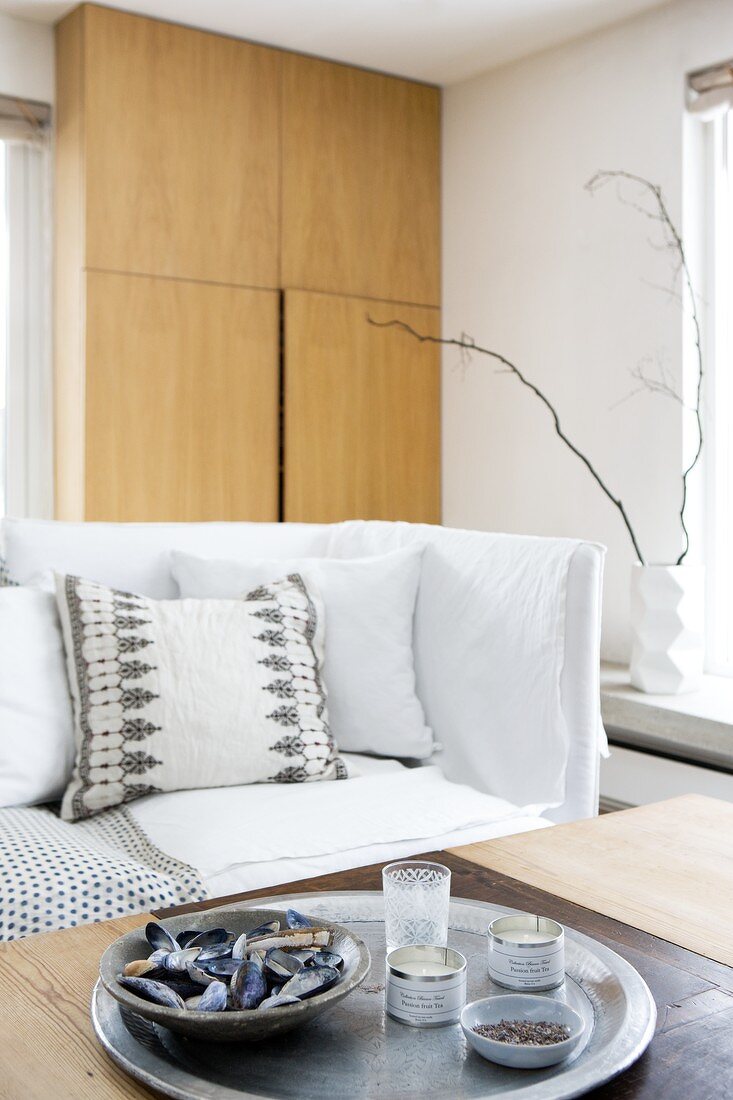 Schale mit Miesmuscheln auf Tablett vor Sofa mit Decken und Kissensammlung; Wandschrank im Hintergrund