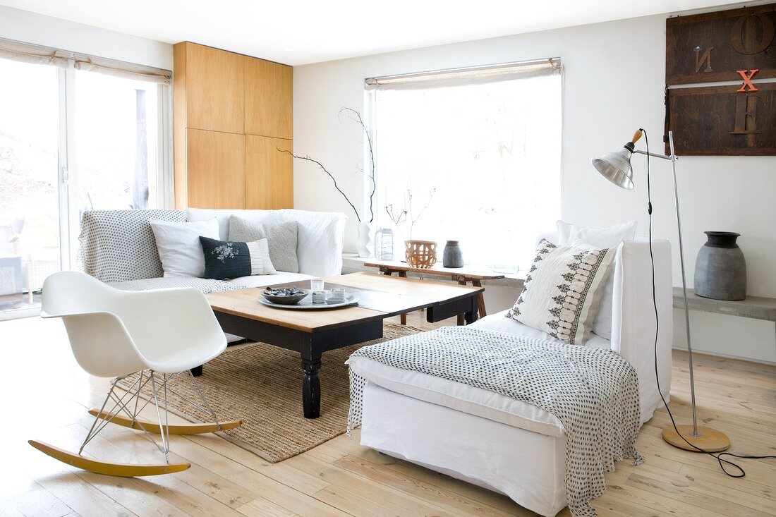 Zwei gemütliche Liegesofas mit Kissen und Decken und Klassiker Schaukelstuhl um einen grossen Holztisch in skandinavischem Wohnzimmer