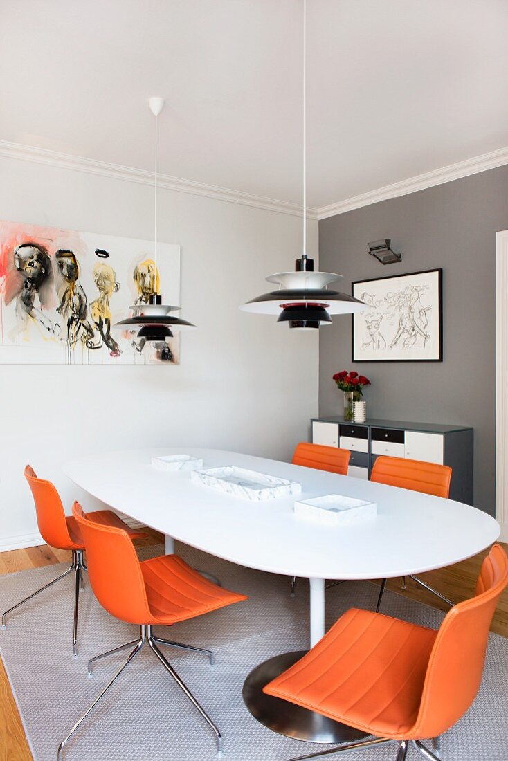 Poulsen Pendelleuchten über weißem Esstisch und Drehstühle mit orangem Lederbezug in Zimmerecke mit grauer Wand