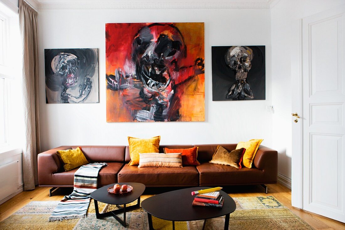 Loungebereich mit schwarzen Metall Couchtischen vor braunem Ledersofa, an Wand expressive Gemälde