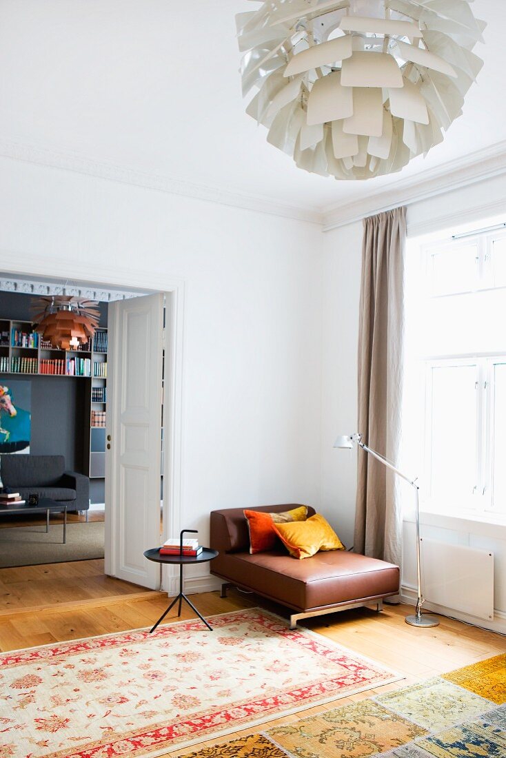 Patterned rug on parquet floor and brown leather armchair in corner between window and open double doors