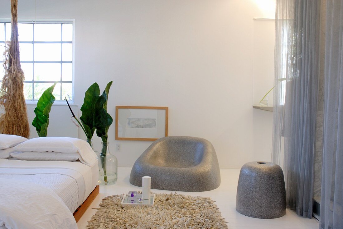 Doppelbett mit asiatischem Flair und Designer Sitzmöbeln in grau vor weißer Wand