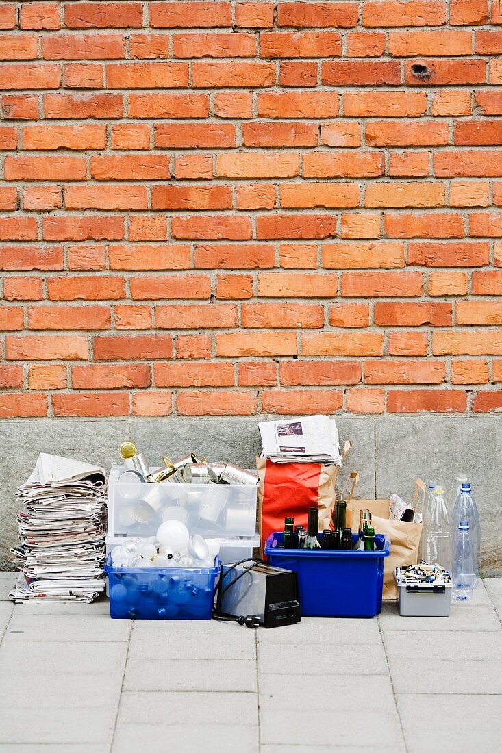 Zeitungen, Flaschen und alter Toaster, für die Wertstoffsammlung gestapelt vor einer Hauswand