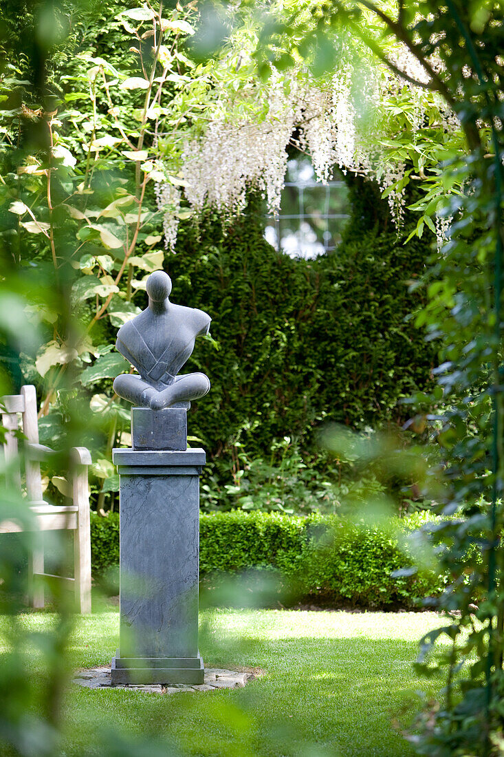 Moderne Skulptur auf Stele in angelegtem Garten
