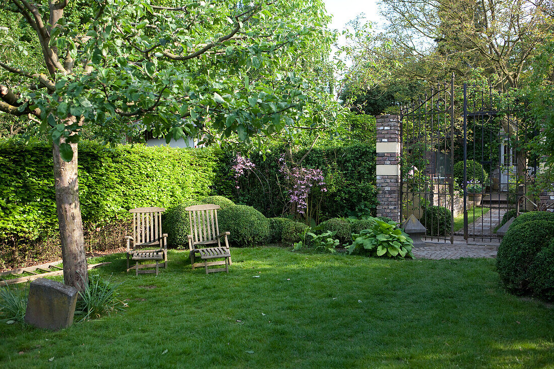 Zwei Holzliegestühle in idyllischem eingewachsenem Garten mit Rasen und Zugang zu Vintage-Gartenhäuschen