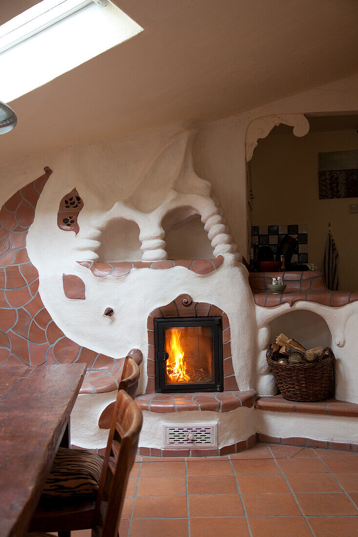Stove and fireplace surround modelled in organic forms with terracotta tiles in open-plan kitchen-dining room of rustic holiday apartment