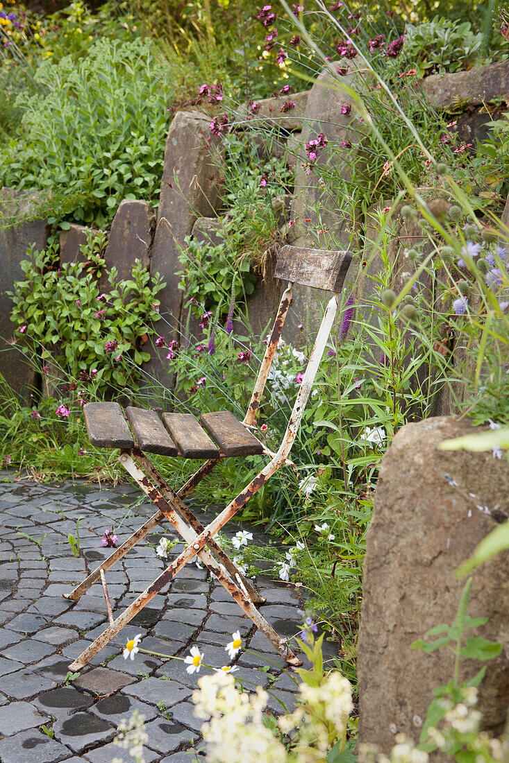 Rostiger Gartenstuhl mit Holz Sitzfläche auf grauem Pflasterboden im Garten