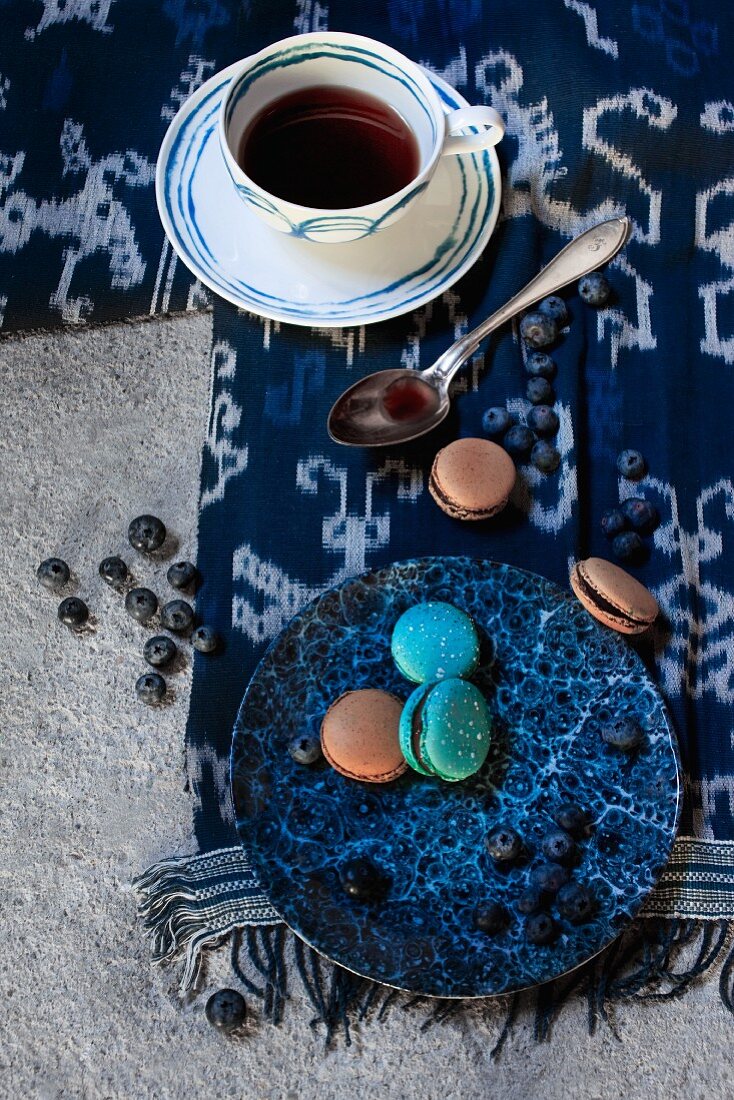Kaffeetasse mit blauem Kreismuster und Teller mit Makronen auf blau-weißem Tuch