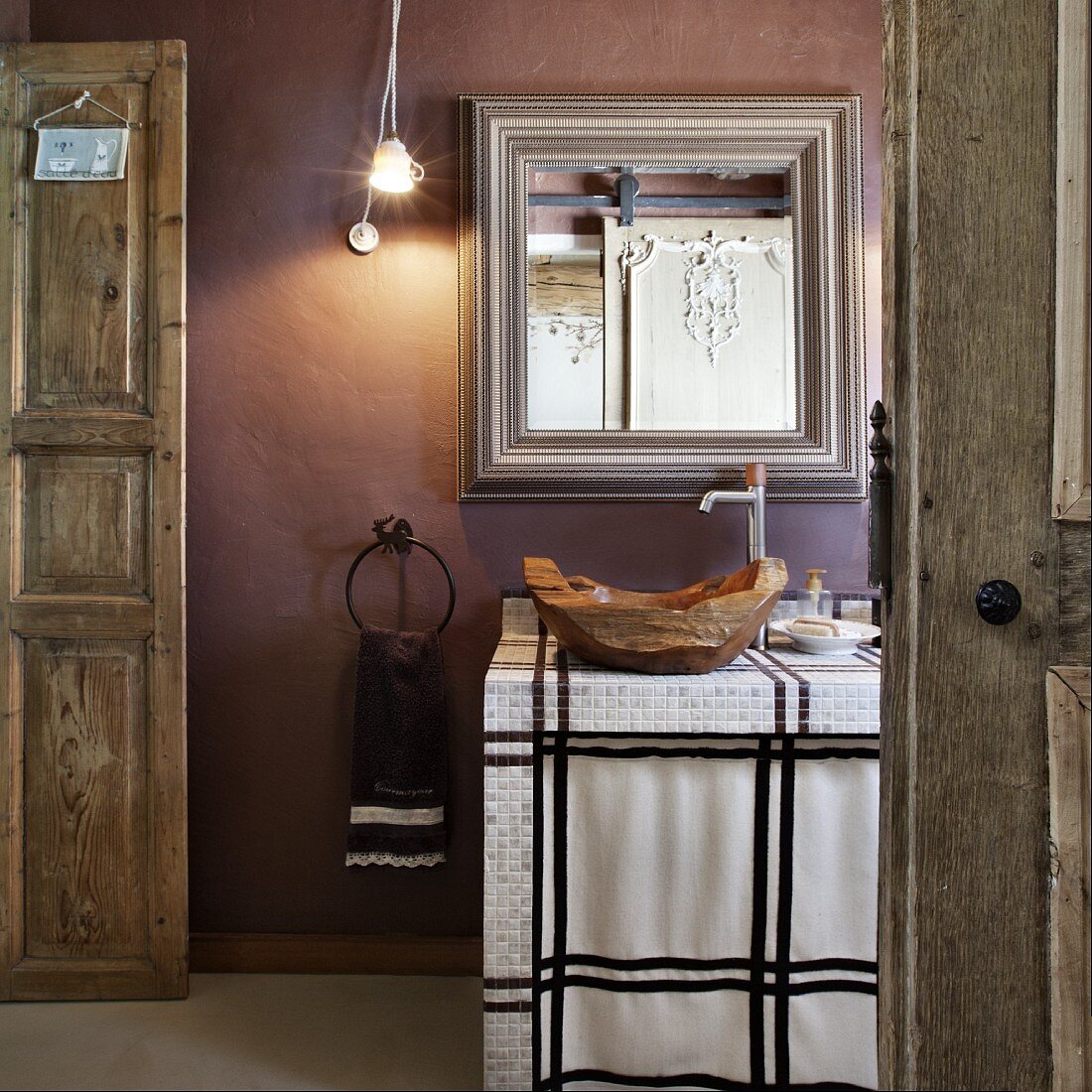 Einblick in ein rustikales Bad - Holzschale als Waschbecken auf gefliestem Waschtisch vor Spiegel an mauvefarbener Wand