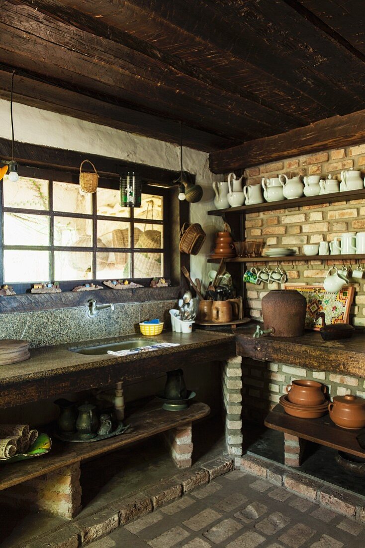 Rustikale Küche mit Ziegelmauern; Tongefässe und weisses Geschirr auf Borden an Ziegelwand