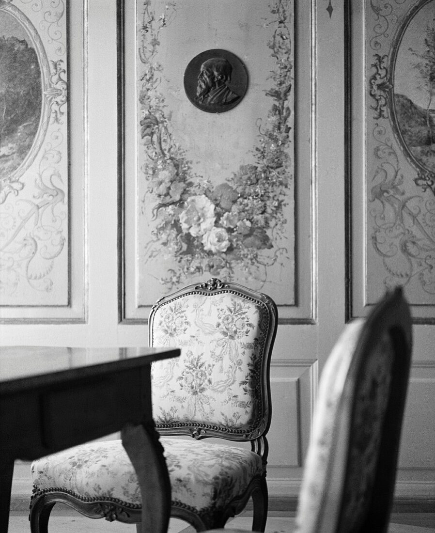 Elegante Stühle vor holzverkleideter Wand mit aufgemalten Blumengirlanden
