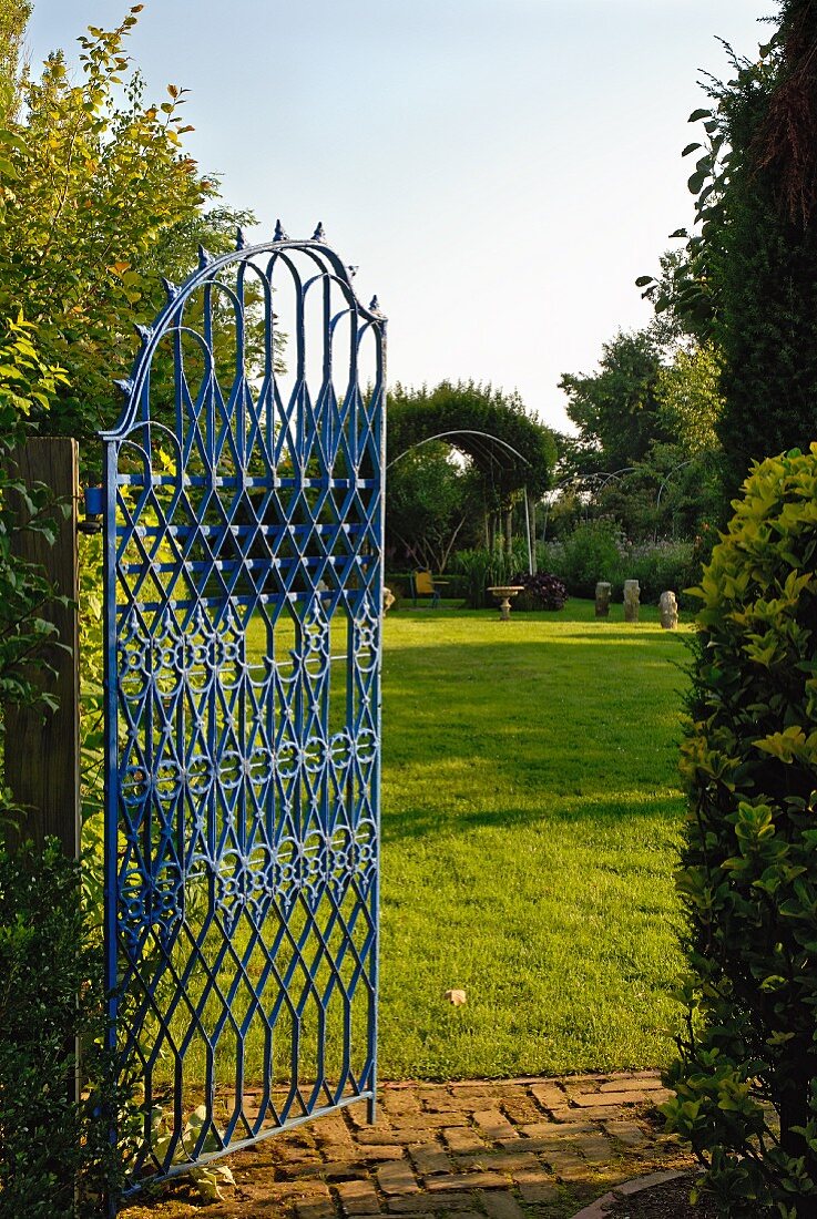 Open, blue iron gate showing view of expansive garden