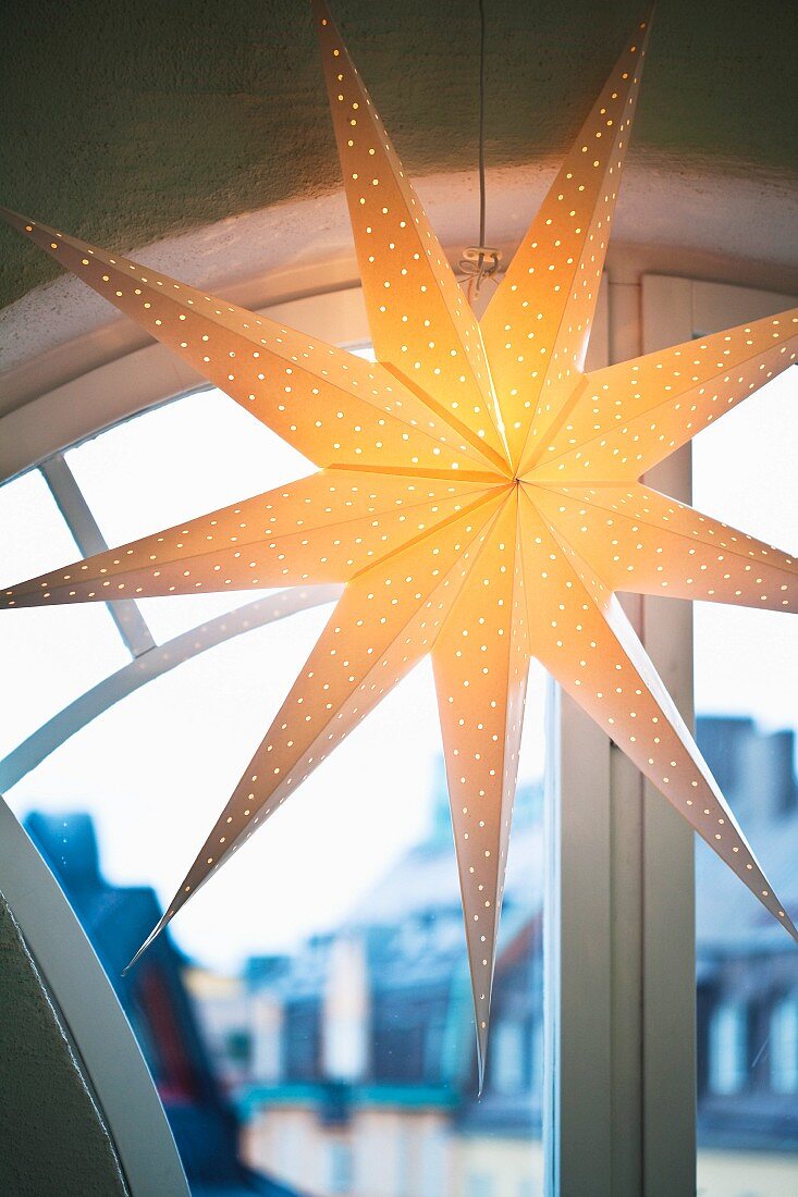 Beleuchteter Weihnachtsstern aus Pappe vor einem Rundbogenfenster