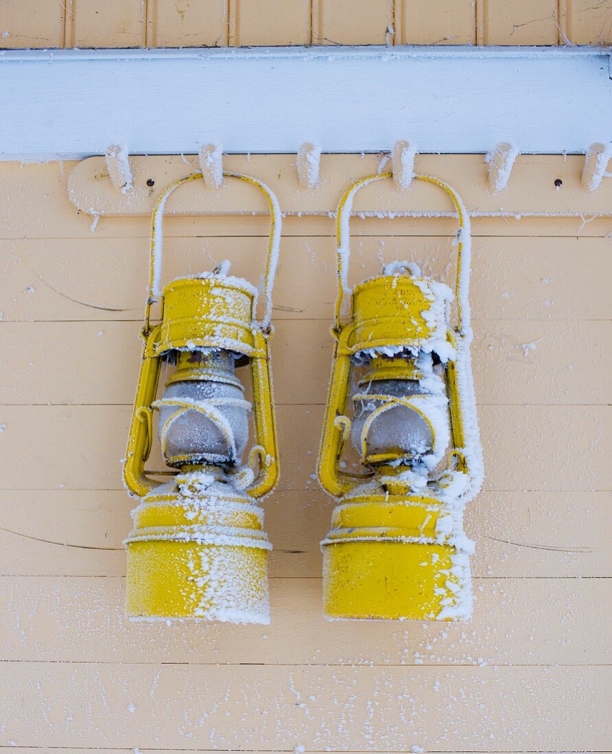 Two snowy lanterns hanging from coat pegs on wooden facade